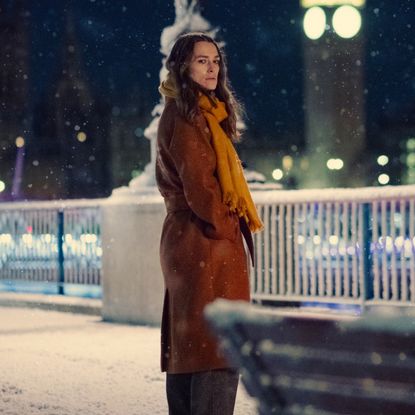 keira knightley stands on a snowy street in an orange coat in black doves