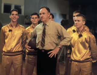 young basketball players in bomber jackets and their coach stand on a high school court in hoosiers