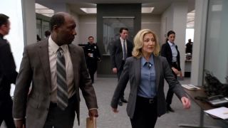 Edie Falco wears a suit and walks through a detective office in Tommy