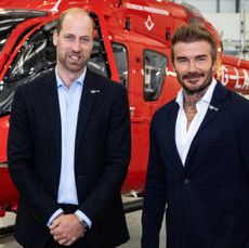 Prince William and David Beckham smiling in front of a helicopter