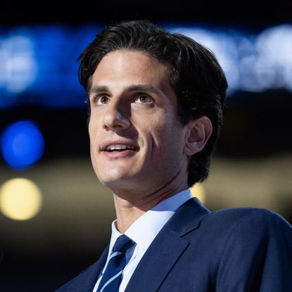 Jack Schlossberg stands onstage at the 2024 Democratic National Convention wearing a dark blue suit with a striped tie, and Kate Middleton wears a wide-brimmed red hat with a matching bright red dress while standing with husband Prince William