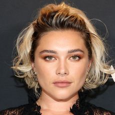 A closeup shot of Florence Pugh wearing a black lace dress and wavy blond hair