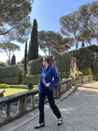 Erika veurink in a blue top, black pants, and black Rothy's mary jane flats looking away in a garden