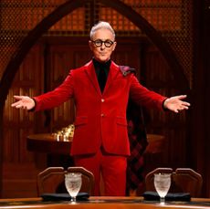 alan cumming poses with his arms outstretched in front of an empty round table, in 'the traitors' season 2