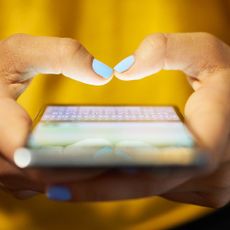 Lady with turquoise nails wearing a mustard sweater busy on a mobile phone