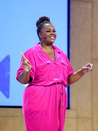 nicole byer wears a pink jump suit on stage at a why wont you date me podcast event