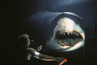 a man underwater approaches a shark as it opens its teeth in the movie Deep blue sea