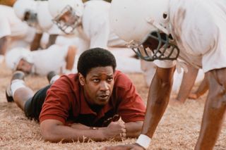 denzel washington lays on the field while talking to football players in remember the titans