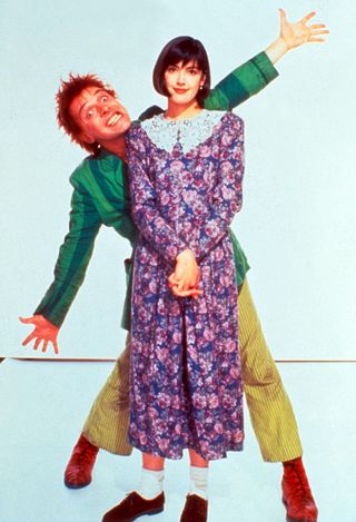 a man in a green suit jacket poses behind a woman in a floral dress in the movie Drop dead fred