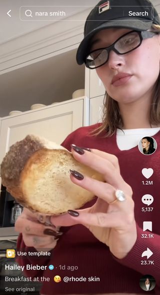 A photo of Hailey Bieber eating bread with deep burgundy red nails