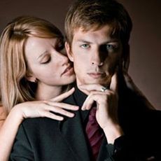 man in suit with woman behind him nuzzling his neck