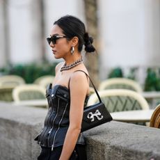 Yoyo Cao wears a black shoulder bag, black sunglasses, silver earrings, a silver large chain necklace, a black shiny leather heart-neck / shoulder-off zipper corset top, black suit pants, outside Cecilie Bahnsen, during Paris Fashion Week - Womenswear Fall Winter 2023 2024, on March 01, 2023 in Paris, France.