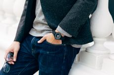 Man resting against a wall with his hand in his pocket, revealing a black & white watch on wrist