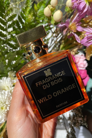 Wild Orange Eau De Parfum in front of an array of colorful flowers.