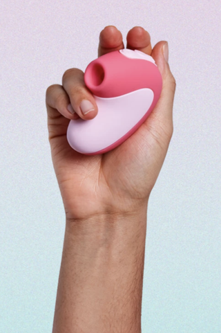 hand holding up a pink suction vibrator on a pink and blue ombre background