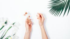 Hands taking the lid off one of the best women's perfumes against a white background with green flowers and leaves