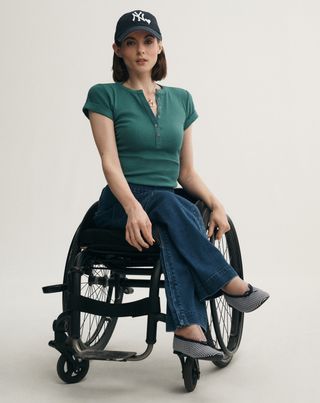 a woman sits in a wheelchair wearing adaptive clothes by anthropologie including jeans a polo shirt and a baseball cap