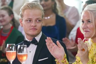 Marius Borg Hoiby wearing a tux sitting at a dinner table next to his mother, Crown Princess Mette-Marit, who is smiling and clapping