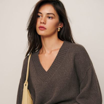 model wearing Reformation Jadey Cashmere Oversized V-Neck Sweater, gold earrings, tan shoulder bag 