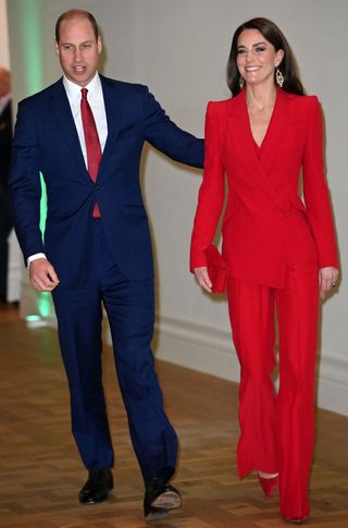 Prince William putting his arm around Kate Middleton wearing a red suit