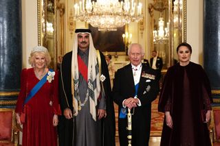 Queen Camilla wearing a tiara and red gown next to the Amir of Qatar and King Charles