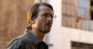 glen powell wears a disguise of glasses and a green shirt in hit man