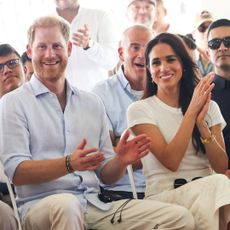 Prince harry and Meghan Markle sitting in a row of chairs clapping and smiling 