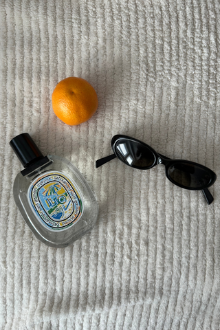 diptyque ilio next to cat eye sunglasses and an orange