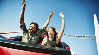 Laughing couple with arms raised riding roller coaster