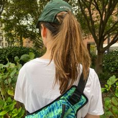 editor Halie LeSavage stands in New York City with her back to the camera wearing a belt bag with a baseball cap and a ponytail