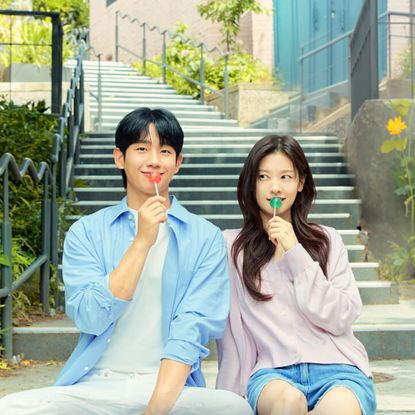 Jung Hae-in and Jung So-min, holding lollipops to their mouths while sitting on outdoor stairs, in the k-drama 'Love Next Door'