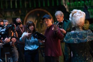 Director of Photography Alice Brooks (center left) and Director Jon M. Chu (center right) discuss a shot as cameramen stand to their left and the cast of 'Wicked' (Jeff Goldblum, Michelle Yeoh, and Cynthia Erivo) stand to their right.