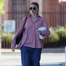 Margot Robbie wearing an oversized red and white button down with baggy blue jeans, sunglasses, and a black shoulder bag