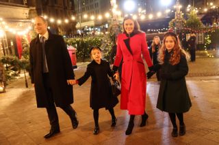 Freddie Windsor, Sophie Winkleman holding hands with their two children with lit Christmas trees behind them as they walk into Westminster Abbey