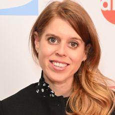 Princess Beatrice wearing a black jacket and polka dot dress smiling at the camera 