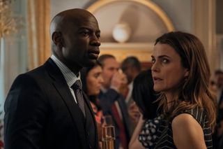 David Gyasi as Austin Dennison, Keri Russell as Kate Wyler, standing in a grand room filled with other people, in episode 203 of The Diplomat.