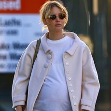 Jennifer Lawrence walking in Los Angeles wearing a pink jacket with black pants and the row's boat shoes