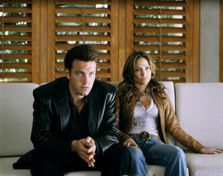 ben affleck in a leather jacket sitting next to jennifer lopez on a couch in the movie Gigli