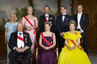 King Harald, Queen Sonia, Princess Ingrid Alexandra, Crown Princess Mette-Marit, Crown Prince Haakon, Prince Sverre Magnus, Marius Borg Hoiby wearing tuxes and evening gowns for a formal portrait in front of a wall covered in tree print wallpaper