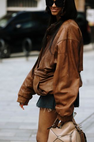 A woman at Paris Fashion Week wears a brown leather bomber jacket with a gray mini skirt.