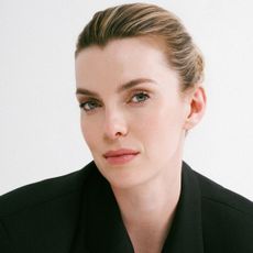 betty gilpin poses in a black blazer and pink lip