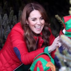 Kate Middleton wears a bright red puffer jacket as she poses with a Christmas tree and elf hats and King Charles laughs next to someone dressed as Santa Claus