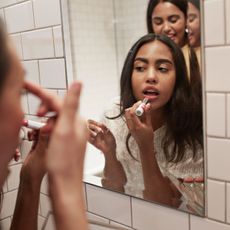 Woman applying lipstick while reflecting in mirror 