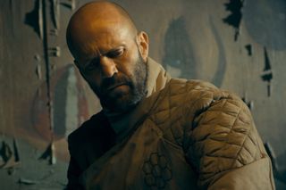 jason statham wears a jacket while looking confused in a seedy building in the beekeeper