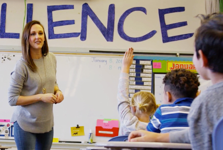 Student raising her hand in class with engaged teacher responding