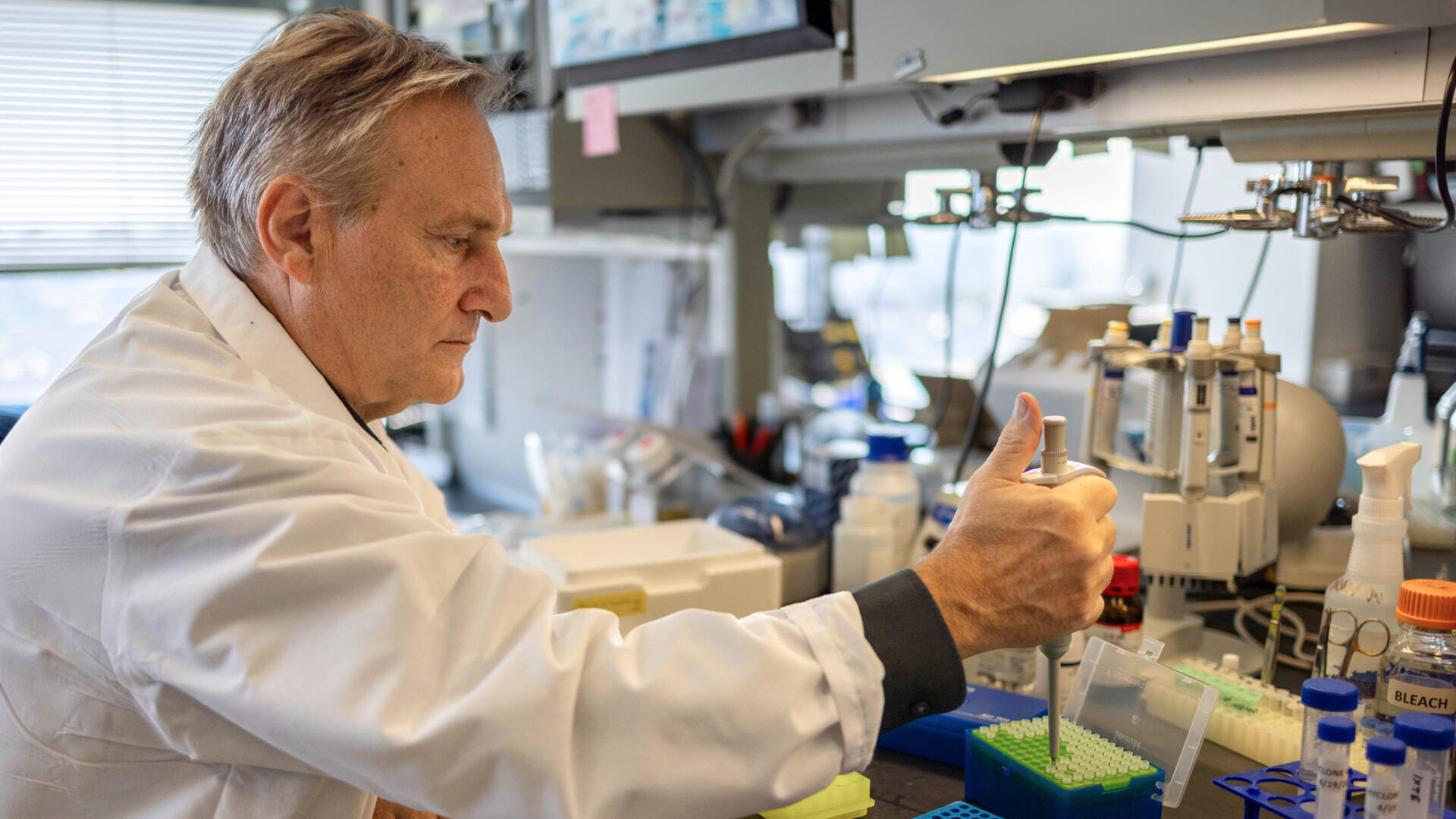 Chan Zuckerberg Biohub New York President Andrea Califano sits at a lab bench with his right arm outstretched and his hand holding a pipette.