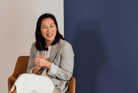 Priscilla Chan sits in an armchair on stage and clasps her hands. She smiles out at the audience.