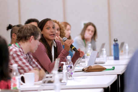 Christina Towers, PhD is seated and holding a microphone while speaking to a group of Science Diversity Leadership grantees.