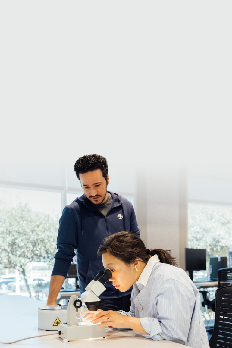 Priscilla Chan looks into a microscope while a colleague observes her in a well-lit laboratory at the CZ Imaging Institute.