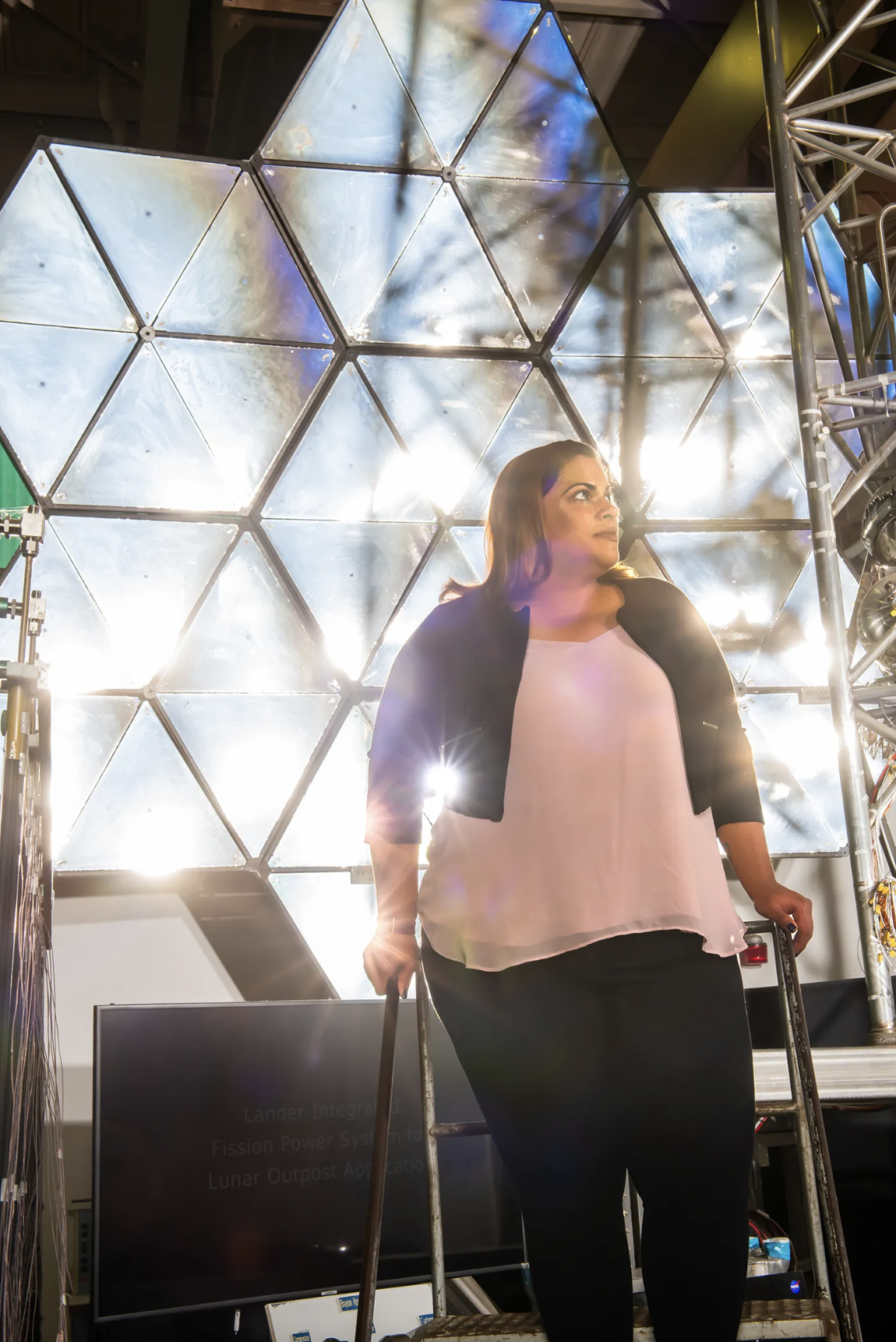 Abigaíl Rodríguez posa frente al espejo del concentrador en el Laboratorio de Propulsión y Energía Eléctrica del Centro de Investigación Glenn de la NASA. Hispana/Latina de la NASA.